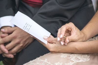 Midsection of bride holding ring and paper with text while sitting by groom