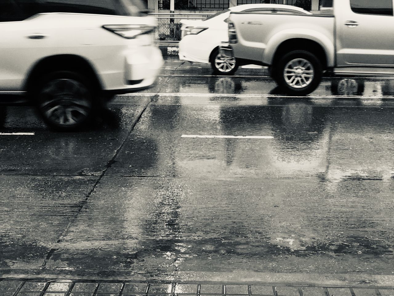 transportation, mode of transportation, motor vehicle, car, land vehicle, city, street, wet, black, rain, wheel, road, black and white, motion, day, monochrome, tire, architecture, vehicle, monochrome photography, white, outdoors, water, no people, automotive exterior, city street