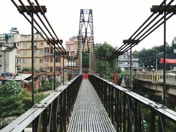 Metallic footbridge in city against sky