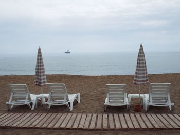 Lounge chairs with umbrellas at beach against cloudy sky
