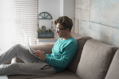 Side view of man using laptop while sitting on sofa