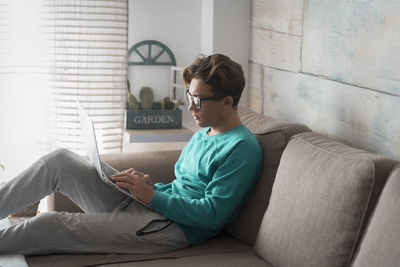 Side view of man using mobile phone while sitting on sofa