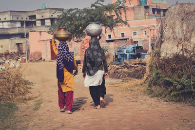 Women walking on street carrying water pot on their head