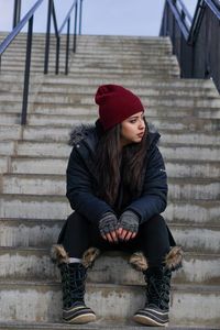 Full length of young woman looking away while sitting on staircase