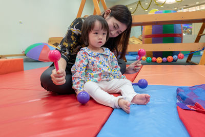 Cute girl with teacher playing on carpet in kindergarten