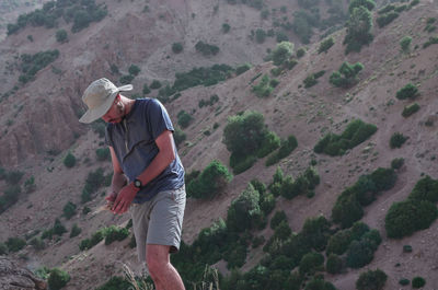 Young man looking down while standing against mountain