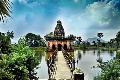 Empty footpath leading towards historic temple on lake against sky