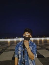 Portrait of young man standing against illuminated light at night