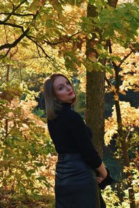 Young woman standing by tree against plants