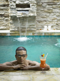 Portrait of shirtless young man wearing sunglasses while swimming in pool