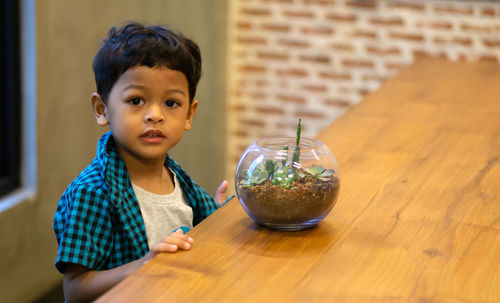 Portrait of cute boy sitting by potted plant on table