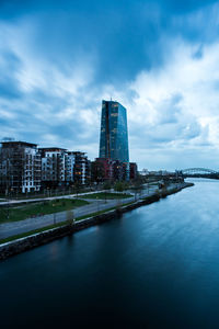 View of buildings by river against cloudy sky
