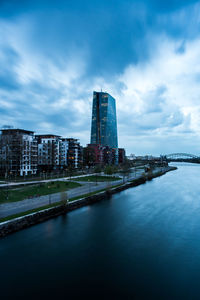 View of buildings by river against cloudy sky in frankfurt, germany 