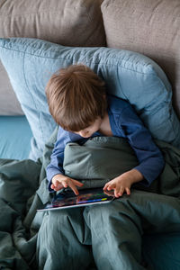 Boy laying in bed and communicating with grandma via video chat using laptop during coronavirus