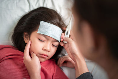 Cropped hand holding thermometer while girl resting on bed