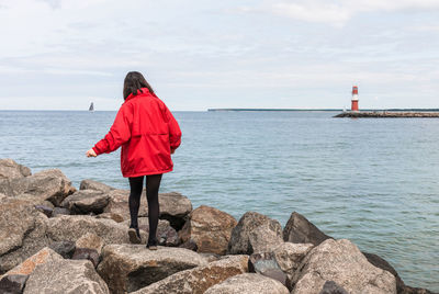 Rear view of man standing on rock by sea against sky