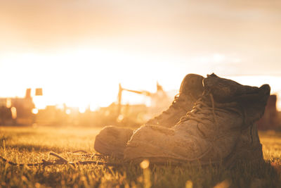 Close-up of shoes on field against sky during sunset