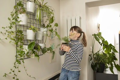 Girl hanging plant on wall at home