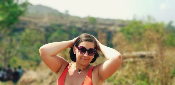 Portrait of young woman wearing sunglasses standing against trees