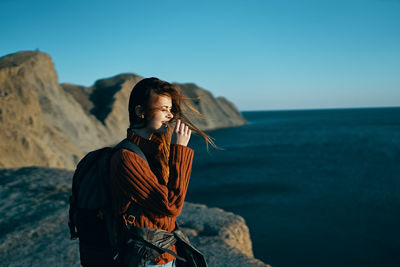 Man standing on rock by sea against sky