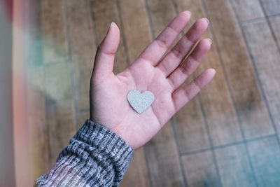 Cropped hand of woman holding heart shape decoration over wooden floor
