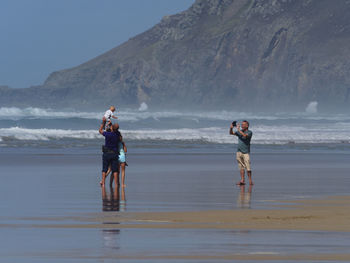 Family standing at beach against mountain
