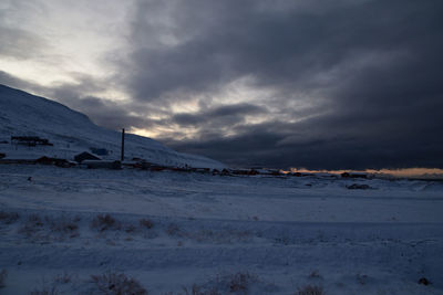 Snow covered land and mountains against sky during sunset