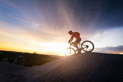 Man riding bicycle on street against sky during sunset