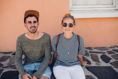 Portrait of smiling friends sitting against wall