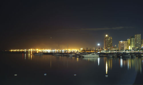 Illuminated city by sea against sky at night