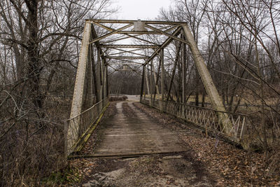 Footbridge over bare trees against sky