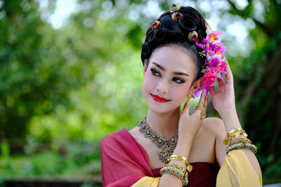 Close-up of thoughtful model in traditional clothing wearing flowers against trees