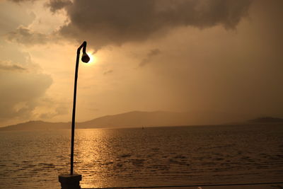 Silhouette street light by sea against sky during sunset