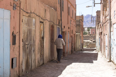 Rear view of man walking on footpath amidst buildings