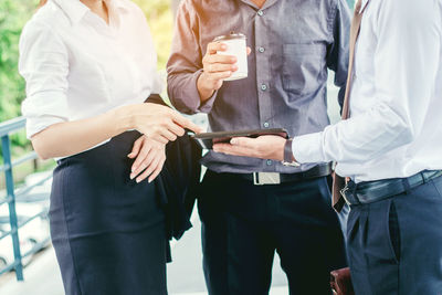 Midsection of business people discussing over digital tablet while standing outdoors