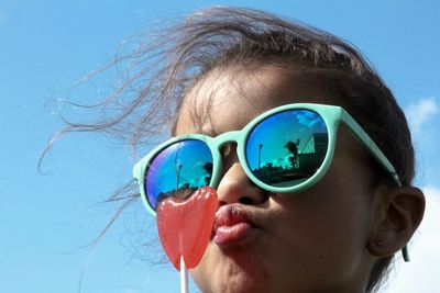 Girl wearing sunglasses with lollipop against sky