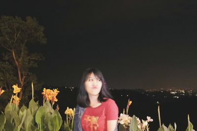 Portrait of woman standing on red flowering plants at night