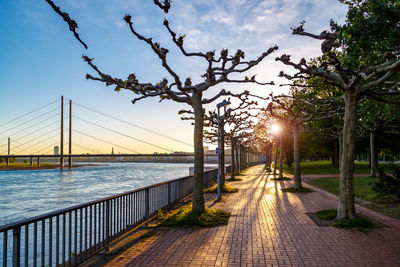 Footpath by railing against sky during sunset