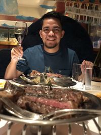 Portrait of a smiling young man drinking glass at restaurant