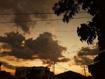 Low angle view of silhouette birds on electricity pylon against dramatic sky