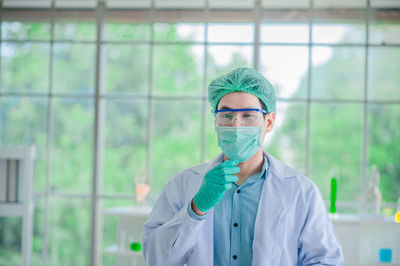 Portrait of scientist wearing surgical mask and cap standing in laboratory