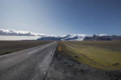 Road leading towards snowcapped mountains against sky