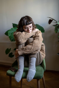 Depressed unhappy teen girl sitting alone at home with knees embraced looking indifferently on floor