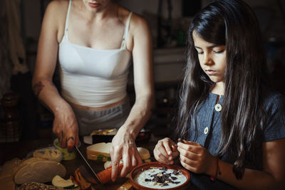 Mother and daughter preparing breakfast while standing in kitchen at home