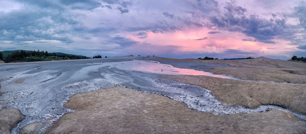 Scenic view of land against cloudy sky during sunset