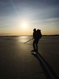 Silhouette man holding ice rod on frozen lake against sky