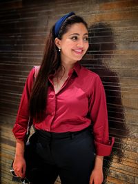 Portrait of smiling young woman standing against wall