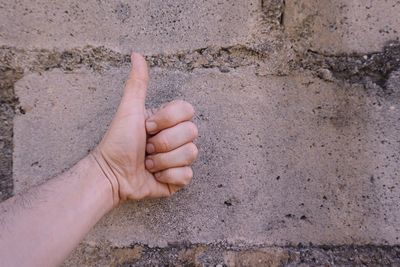 Close-up of hand gesturing thumbs up against wall outdoors