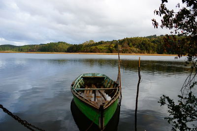 Boat moored in river against cloudy sky