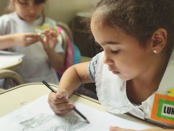 Girl with name tag drawing on paper at desk in school